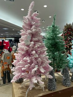 there is a pink christmas tree in the middle of this store display with other trees behind it