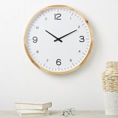 a white clock on the wall next to a stack of books and a vase with glasses