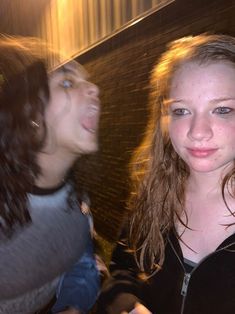 two young women standing next to each other in front of a brick wall with their mouths open