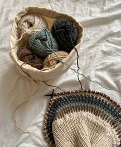 a basket filled with balls of yarn next to a knitted bowl on top of a bed