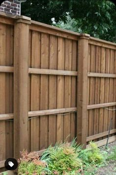 a wooden fence next to a brick building and green plants on the side of it