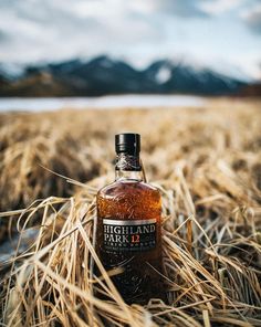 a bottle of highland park 12 is sitting in the middle of a field with mountains in the background