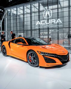 an orange acura sports car on display in a showroom with people looking at it