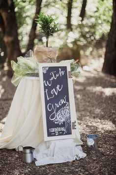 a chalkboard sign sitting on top of a white blanket next to a potted plant