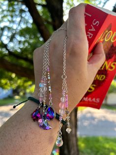 a person is holding up a book in their hand while wearing bracelets with charms