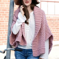 a woman wearing a pink knitted shawl and hat standing next to a pole