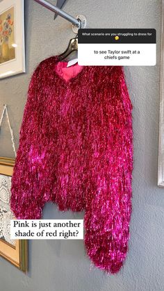 a pink fuzzy sweater hanging on a wall next to a framed photo and an empty hanger