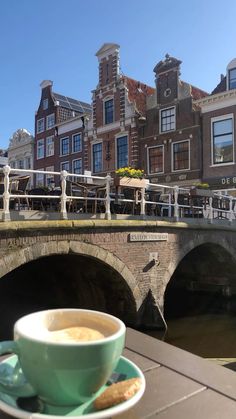 a cup of coffee sitting on top of a saucer next to a bridge with buildings in the background