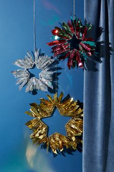 three christmas decorations hanging from strings against a blue wall with curtains in the foreground