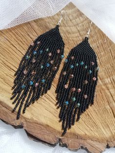 black beaded earrings with multi - colored beads are on a piece of drift wood