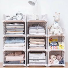 a white shelf filled with lots of folded clothes and a stuffed animal sitting on top of it