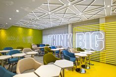 an office with yellow and blue chairs and tables in front of a neon sign that reads think big