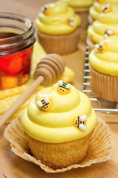 cupcakes with yellow frosting and bees on them, next to honey jars