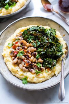 mashed potatoes topped with spinach and black eyed peas on a white plate next to silver spoons