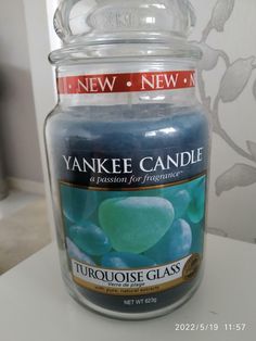 a yankee candle is sitting on a counter next to a glass jar with blue and green candies in it