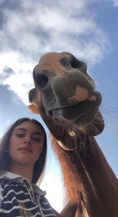 a woman standing next to a brown and white giraffe under a cloudy blue sky