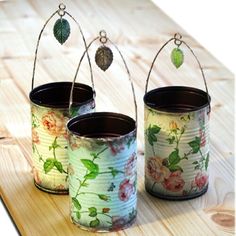 three tins with flowers painted on them are sitting on a wooden table and one is hanging from a wire