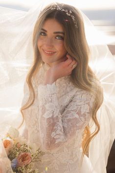 a woman wearing a wedding dress and holding a bouquet in front of her face, smiling at the camera