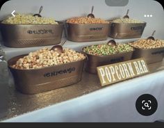 several metal buckets filled with different types of popcorn on top of a white table