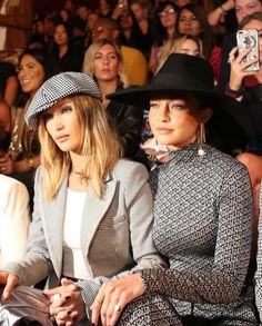 two women sitting next to each other in front of a group of people wearing hats