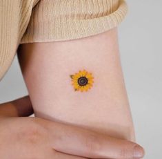 a small sunflower tattoo on the side of a woman's right arm