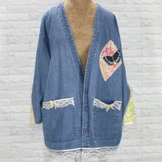 a blue jean jacket with patches and laces on the side, hanging against a white brick wall