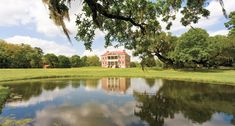 a large house sitting on top of a lush green field next to a lake in front of it