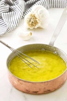 a pot filled with yellow liquid next to garlic and a whisk on the side