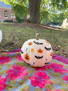 a painted pumpkin sitting on top of a blanket in the middle of a yard next to a tree