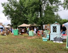 many people are standing around at an outdoor flea market with tables and chairs in front of them