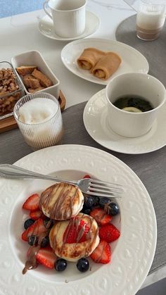 a plate with pancakes, strawberries and blueberries on it next to cups of coffee