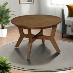 a round wooden table sitting on top of a rug in front of a couch and potted plant