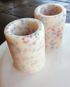 two white vases with colorful sprinkles sitting on top of a plate