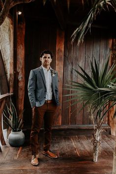 a man standing in front of a wooden wall next to a potted palm tree