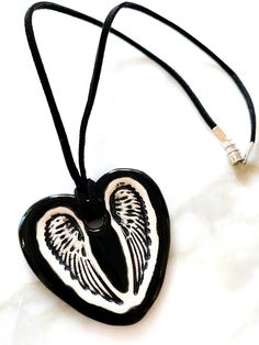 This is a hand-formed and hand painted ceramic heart with wings necklace made by Surly Amy at Surly-Ramics. This necklace has one of our small size pendants.*PLEASE NOTE I make these in small batches so the necklace you receive may vary slightly from the one in the photo. The color, size and style will be the same but the glaze will settle slightly differently from piece to piece.I have posted some photos of one of my models the beautiful Surly Brooke wearing a similar necklace so you can see ho Gift Black Jewelry With Wing-shaped Pendant, Wing-shaped Black Jewelry Gift, Wing-shaped Black Jewelry For Gifts, Black Wing-shaped Jewelry Gift, Black Wing-shaped Jewelry For Gifts, Black Heart-shaped Necklace For Keepsake, Black Heart Necklace For Keepsake, Black Heart Necklaces For Keepsake, Hand Painted White Heart Jewelry