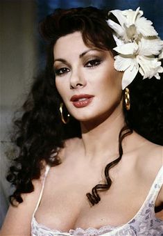 a woman with long dark hair wearing a white dress and flower in it's hair