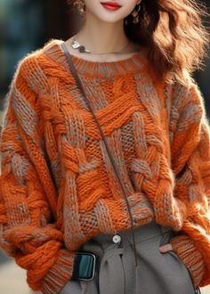 a woman wearing an orange sweater and grey pants with her hand on her hip while looking at the camera