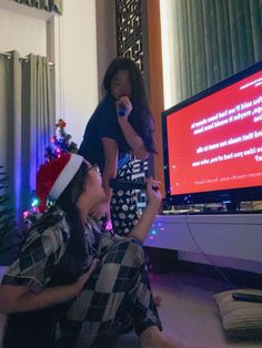 two people sitting in front of a television with a christmas tree on the tv stand