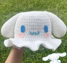 a crocheted elephant hat with blue eyes and ears is held up in the grass