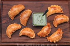 several pastries on a wooden tray with a green dip in the middle and sauce