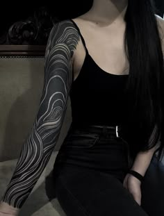 a woman sitting on a couch with her arm covered in black and white tattoos,