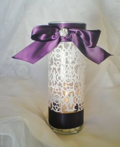 a candle holder with a purple ribbon and lace on the top is adorned with a jeweled brooch