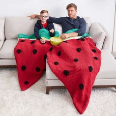 a man and child sitting on a couch with a blanket that has ladybugs on it