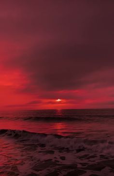 the sun is setting over the ocean with waves crashing in front of it and red clouds