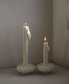 two white candles sitting next to each other in front of a wall and cement floor