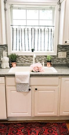 a kitchen with white cabinets and pink flowers in the window sill above the sink