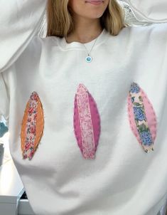 a woman with blonde hair wearing a white sweatshirt with colorful surfboards on the front