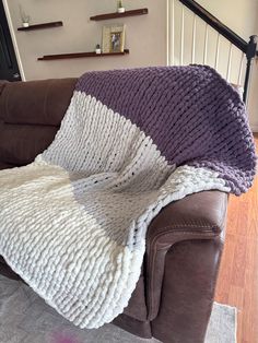 a couch with a purple and white blanket sitting on it's back in a living room