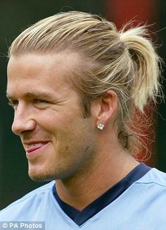 a man with blonde hair wearing a blue shirt and silver earrings smiles at the camera