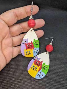 a pair of earrings with colorful cats painted on the front and back of them, hanging from a person's hand